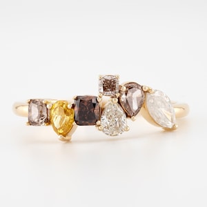 Peut inclure: Une bague en or ornée de pierres précieuses colorées de différentes formes. La bague présente des pierres de taille carrée, poire et marquise dans des tons de marron, jaune et blanc. La bague est posée sur un fond blanc.