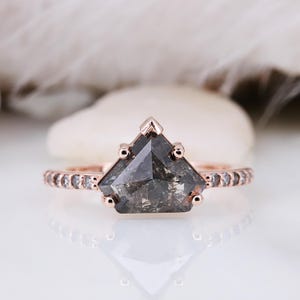 May include: A rose gold engagement ring with a grey, triangular, salt and pepper diamond. The ring has a delicate band with small diamonds set in a pave setting.