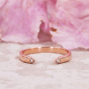 Peut inclure: Une bague ouverte en or rose avec une finition polie et deux extrémités pointues, chacune sertie d'un petit diamant rond transparent. La bague présente un design épuré avec une ouverture au centre, mettant en valeur son éclat métallique.