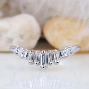 Op de afbeelding: Een zilveren ring met een gebogen band en een rij baguette-vormige diamanten die in een aflopend patroon zijn gezet.