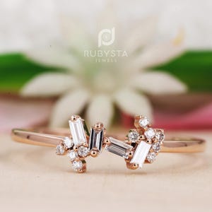 Peut inclure: Une bague en or rose ornée d'un groupe de pierres transparentes taille baguette et taille ronde, disposées en deux ensembles distincts sur l'anneau. Le logo RubySta Jewels est visible en arrière-plan au-dessus de la bague polie.