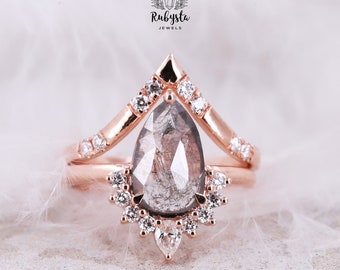 Puede incluir: Un anillo de compromiso de diamante gris en forma de pera engastado en oro rosa con una banda delicada de diamantes más pequeños. El anillo presenta un diseño único y puntiagudo con un racimo de diamantes que rodean la piedra central.