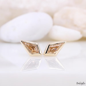 May include: A pair of gold earrings with a diamond-shaped setting and a light brown gemstone in each earring.