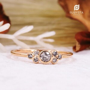 Peut inclure: Une délicate bague en or rose avec un groupe de petits diamants ronds. Le diamant central est plus grand que les diamants environnants.