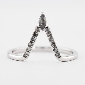 Peut inclure: Une bague en forme de V en métal argenté poli, ornée d'une pierre centrale gris foncé taille marquise à la pointe et d'une série de petites pierres rondes gris foncé serties le long des deux côtés de l'anneau pour un aspect symétrique.
