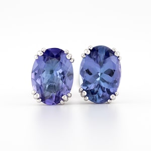 May include: A pair of silver earrings with oval-shaped blue gemstones. The gemstones have a faceted cut and a deep blue color.