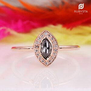 Peut inclure: Une bague en or rose avec un diamant noir de forme marquise entouré d'un halo de diamants plus petits.