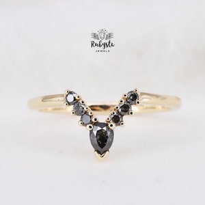 May include: A gold ring with a pear-shaped black diamond in the center and smaller black diamonds on either side, forming a V-shape.