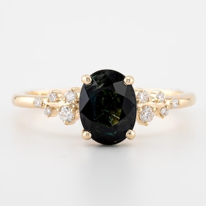 Peut inclure: Une bague en or avec une grande pierre précieuse verte de forme ovale entourée de diamants plus petits. La bague a un design délicat d'inspiration florale.