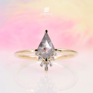 May include: A gold ring with a gray, kite-shaped diamond and a halo of smaller diamonds. The ring is set on a white background.