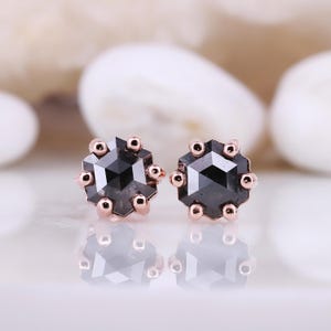 Peut inclure: Une paire de boucles d'oreilles clous en or rose avec des pierres centrales en diamant noir. Chaque pierre est entourée d'un halo de diamants plus petits.