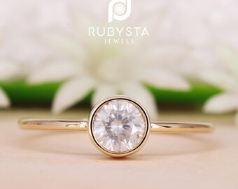 May include: A simple gold band ring with a bezel-set round solitaire diamond.