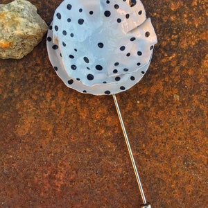 May include: A white ceramic pin with black polka dots. The pin is attached to a silver metal pin back.