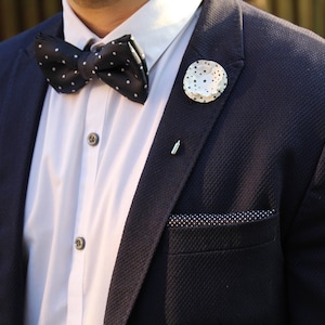 May include: A navy blue suit jacket with a white shirt, a black and white polka dot bow tie, and a white pin with a polka dot design.
