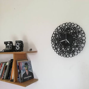 orologio è appeso di fianco ad una mensola con dei libri e delle macchine fotografiche