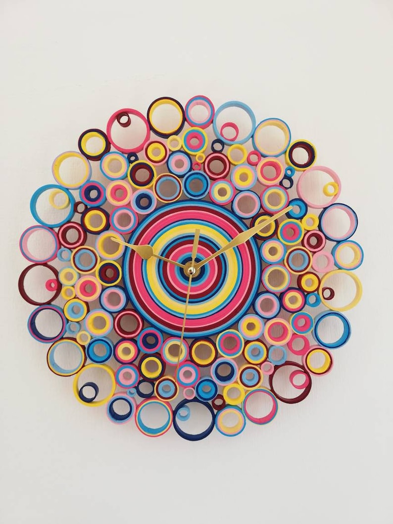 May include: A colorful clock made of paper rolls in shades of pink, blue, yellow, and red. The clock face is a concentric circle design with gold hands.