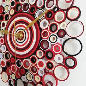 May include: A red, white, and black paper quilling clock with gold hands. The clock face is made of concentric circles of paper.