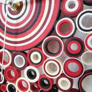 May include: A red, white, and black paper quilling clock with a circular design. The clock face is made of concentric circles of paper, and the hands are silver.