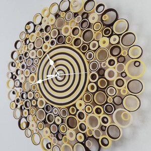 May include: A yellow and brown paper clock with a circular design. The clock face is made of concentric circles of yellow and brown paper. The clock hands are white.