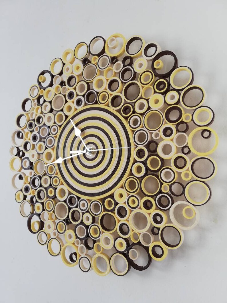 May include: A yellow and brown paper clock with a circular design. The clock face is made of concentric circles of yellow and brown paper. The clock hands are white.