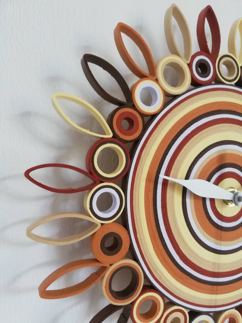 May include: A circular wall clock with a brown, orange, and white concentric circle design. The clock has a white hand and a brown, orange, and white flower design around the outer edge.