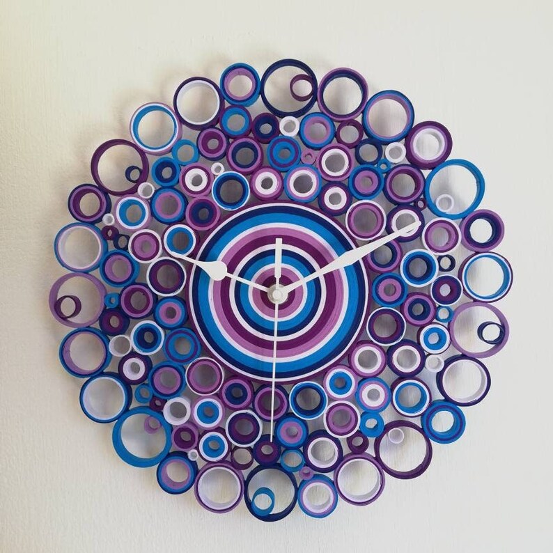 orologio da parete creato con rotolini di carta dai colori viola, glicine, bianchi, turchesi e blu. Le lancette sono bianche (bianche 1) e il diametro è di 28 cm