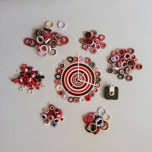 May include: A red, white, and black paper clock with a clock mechanism. The clock is surrounded by a variety of red and white paper circles.