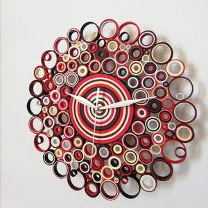 May include: A red, white, and black paper quilling clock with a concentric circle design. The clock face is made of layered paper circles in red, white, and black.