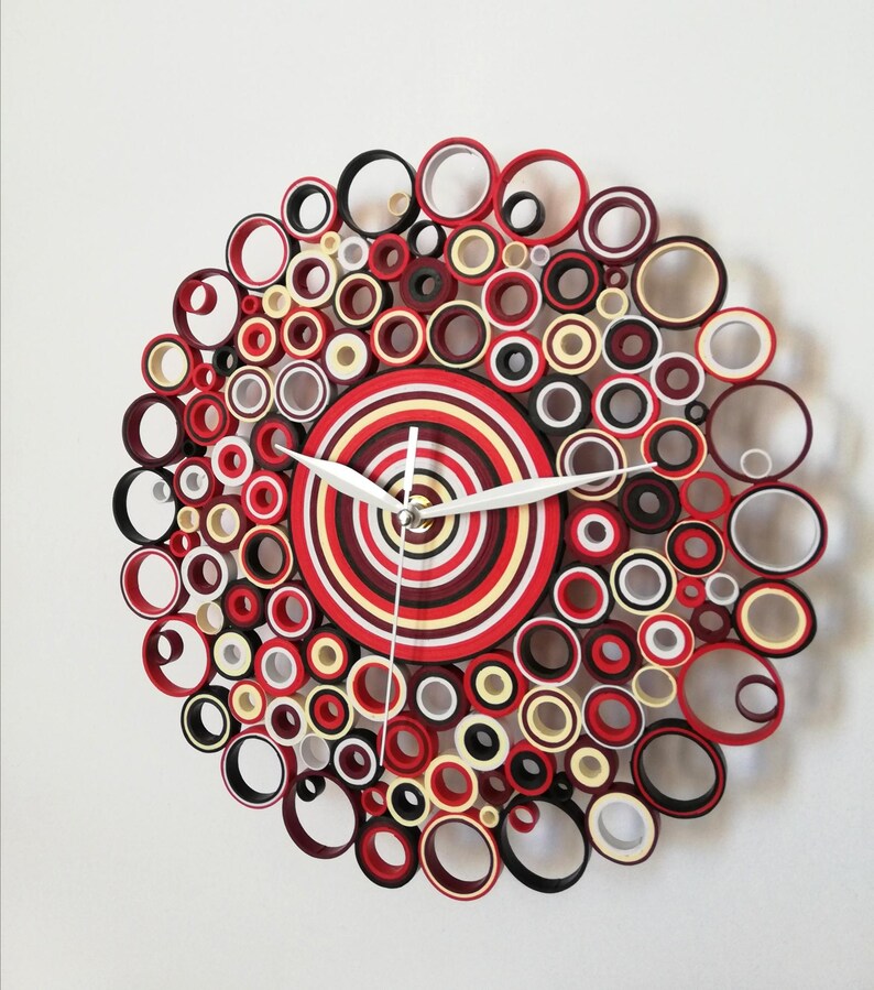 May include: A red, white, and black paper quilling clock with a concentric circle design. The clock face is made of layered paper circles in red, white, and black.