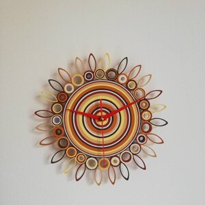 May include: A circular wall clock with a colorful design of concentric circles in shades of brown, yellow, and white. The clock hands are red.