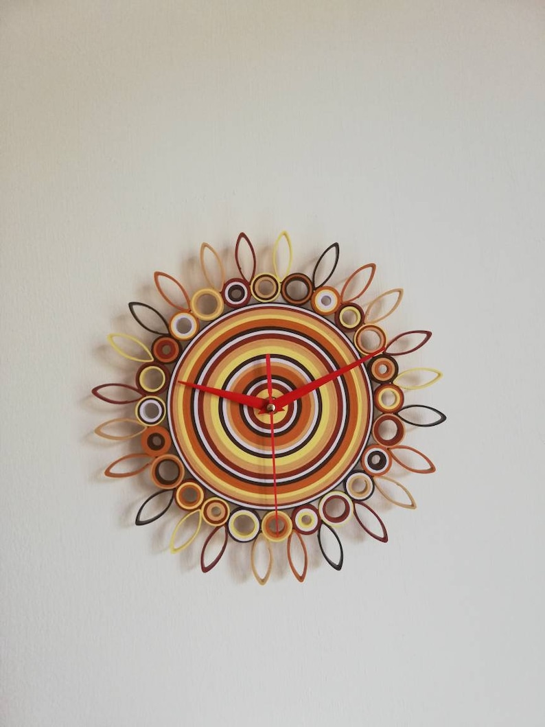 May include: A circular wall clock with a colorful design of concentric circles in shades of brown, yellow, and white. The clock hands are red.