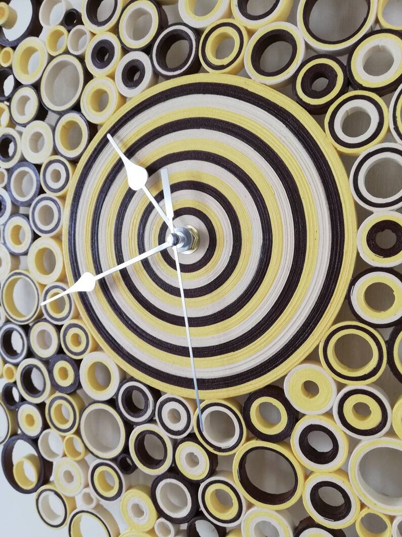 May include: A yellow and brown paper clock with a circular design. The clock face is made of concentric circles of yellow and brown paper. The clock hands are silver.