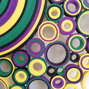May include: A colorful wall art piece made of layered circles of yellow, green, purple, and black paper. The circles are arranged in a random pattern, creating a visually interesting and abstract design.