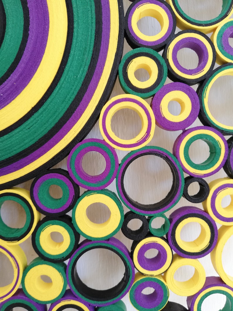 May include: A colorful wall art piece made of layered circles of yellow, green, purple, and black paper. The circles are arranged in a random pattern, creating a visually interesting and abstract design.