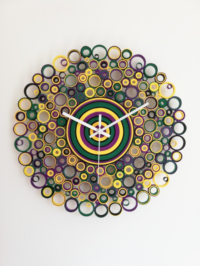 May include: A circular wall clock made of paper rolls, with a concentric circle design in green, yellow, and purple. The clock hands are white.