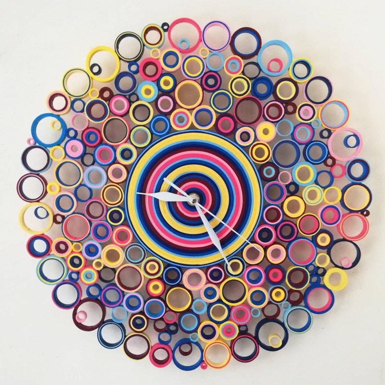 May include: A colorful clock made of paper circles, with a white clock hand. The clock face is a multi-colored spiral design.