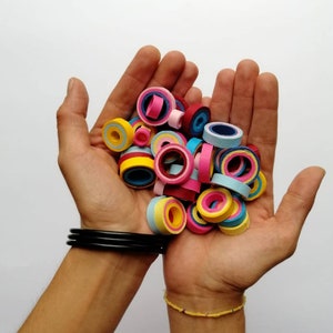 May include: A collection of colorful paper rings in various shades of pink, blue, yellow, and red. The rings are stacked and arranged in a pile, creating a visually appealing pattern.