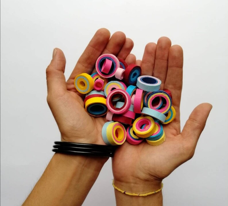 May include: A collection of colorful paper rings in various shades of pink, blue, yellow, and red. The rings are stacked and arranged in a pile, creating a visually appealing pattern.