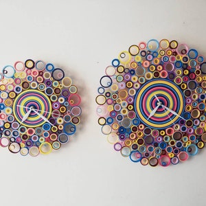 May include: Two colorful clocks made of paper circles, one larger than the other, with white hands and a concentric circle design in the center.