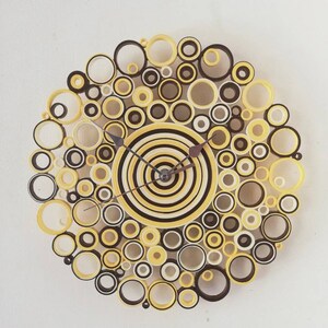 May include: A yellow and black paper quilling clock with a circular design. The clock face is made of concentric circles of yellow and black paper, and the outer edge of the clock is decorated with a ring of smaller circles.