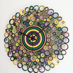 May include: A circular wall clock made of paper rolls, with a layered center in shades of green, yellow, and purple. The clock face is surrounded by a ring of smaller circles in black, yellow, green, and purple.