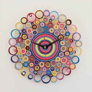 May include: A colorful clock made of rolled paper circles in shades of pink, yellow, blue, and red. The clock face is a concentric circle design with black hands.