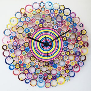 May include: A colorful clock made of paper circles, with a black clock face and hands. The clock is surrounded by a ring of smaller circles in various colors, including pink, blue, yellow, and green.
