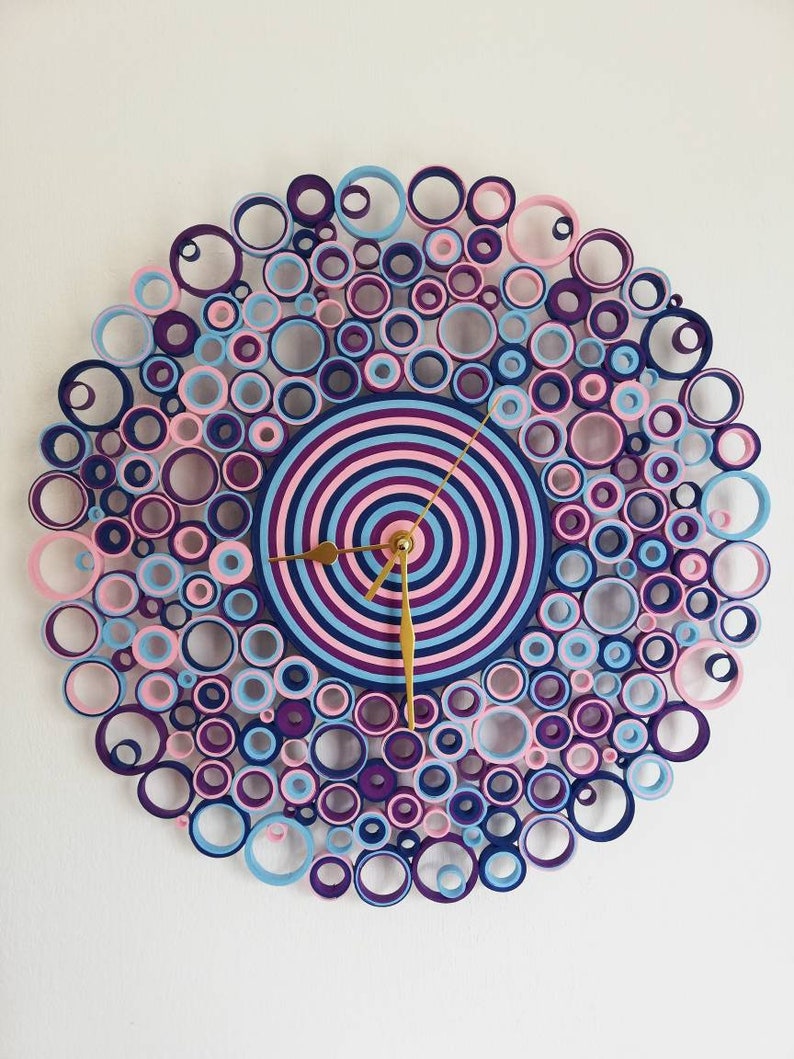 orologio da parete creato con cartoncini rosa, viola, celeste e blu. l'orologio è composto da tanti rotolini dai vari diametri e misura38 cm. le lancette sono dorate.