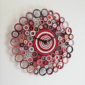 May include: A red, white, and black paper quilling clock with a circular design. The clock face is made up of concentric circles of red, white, and black paper.