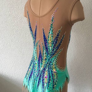 May include: A turquoise and blue leotard with a sheer back and a crystal design. The leotard has a scalloped hem and is decorated with rhinestones.