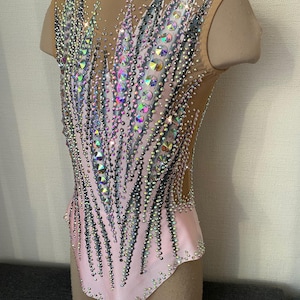 May include: A pink and nude leotard with a dazzling array of iridescent rhinestones and crystals. The sleeveless garment features a mesh overlay and a decorative pattern of sparkling embellishments, creating a glamorous look. The leotard is designed for gymnastics or dance performances.