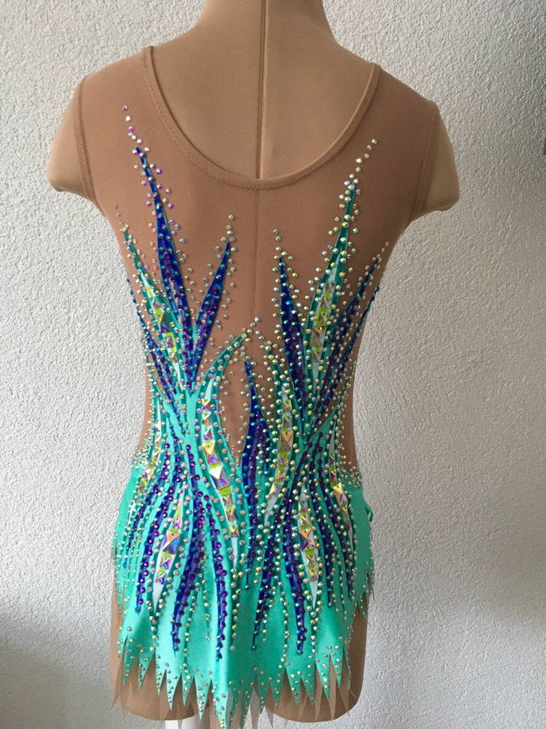 May include: A turquoise leotard with a sheer back and a design of blue and purple rhinestones. The leotard has a scalloped hemline.