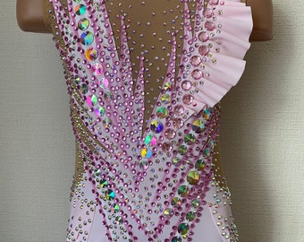 May include: A pink leotard with a mesh back and a ruffled shoulder strap. The leotard is decorated with iridescent rhinestones in a geometric pattern.