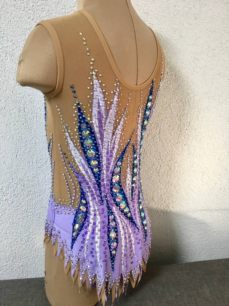 May include: A purple and blue leotard with a geometric design and rhinestones. The leotard has a scoop neck and a sleeveless design.